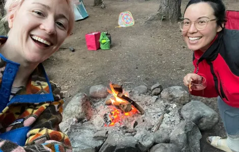 Two mom friends smile for a selfie while camping.
